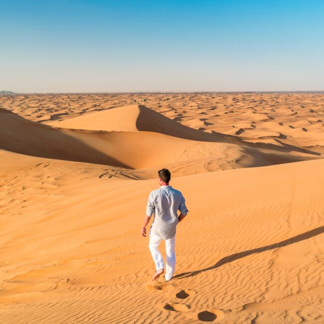 Dubai desert sand dunes, young men walking at the sand dunes of Dubai during a desert safari